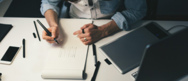 Person mit Stift und Papier am Schreibtisch_Wurster Reichert Nowack
